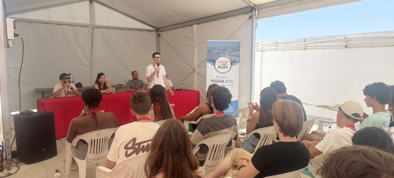 Sessão do projeto Pegada Azul, com orador ao microfone e plateia de jovens sob uma tenda